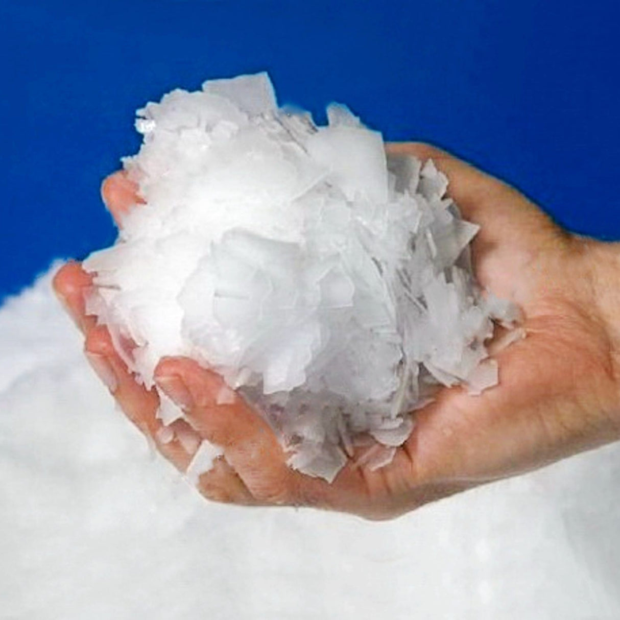 Person holding handful of Flake Ice against blue backdrop.